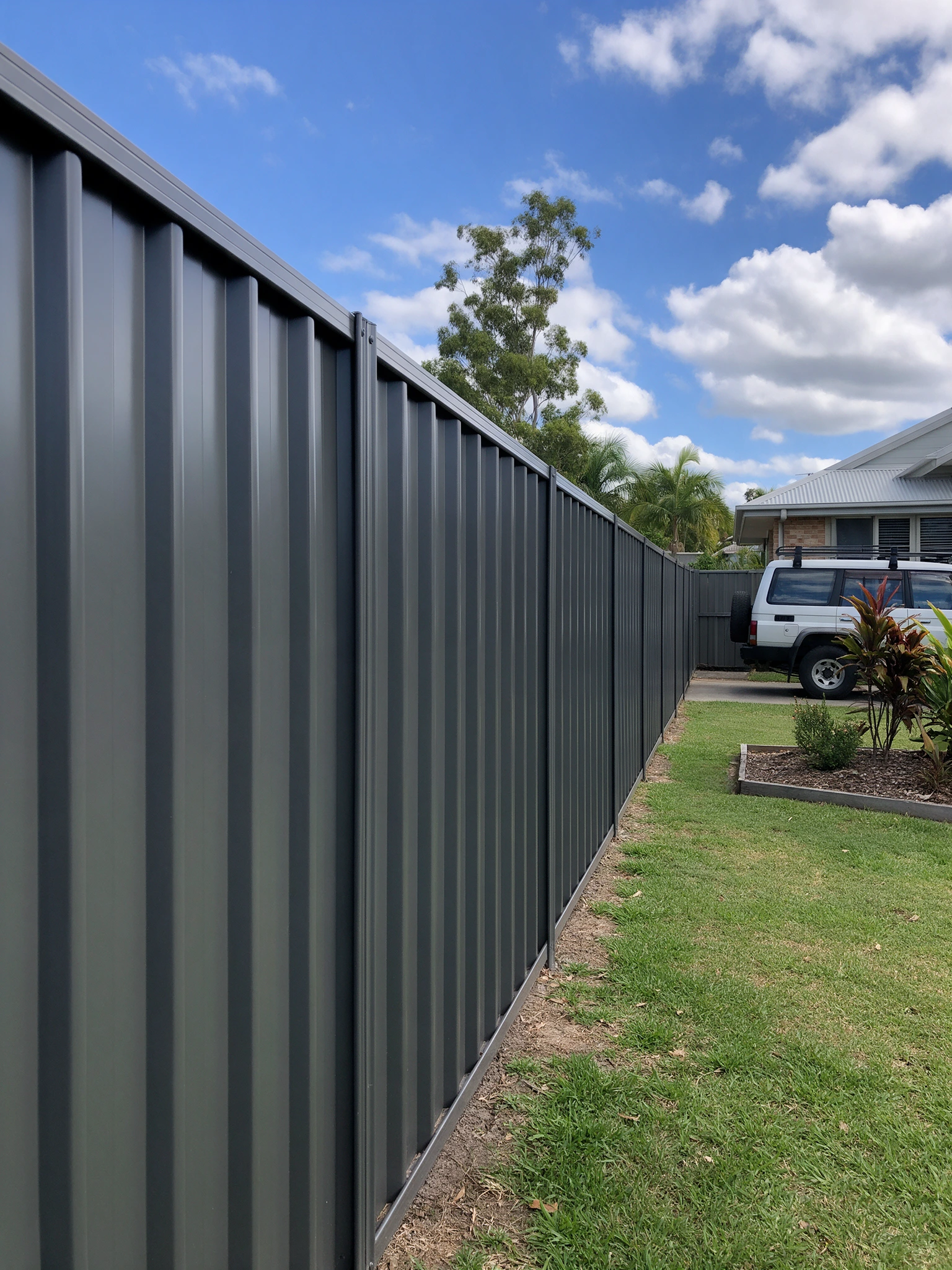 Dark grey steel fence panels running the length of a backyard